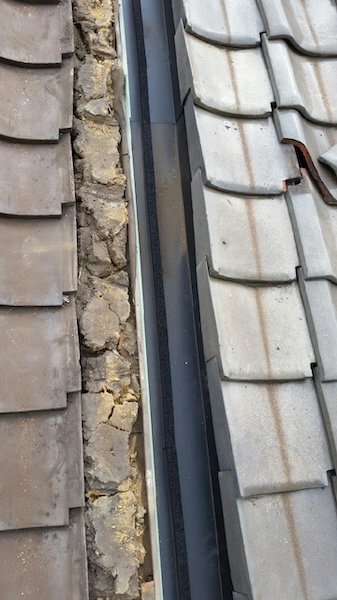 雨漏り原因の特定。幅が狭く排水許容量を超えていた既存の捨て板金と、堆積した土砂の様子