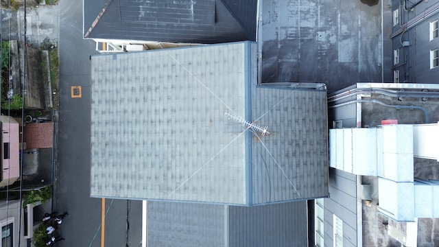 ドローンで真上から撮影したスレート屋根の全景。既存の屋根材の上から新しい防水シートと屋根材（T・ルーフ モダン等）を被せる「カバー工法」の施工計画に使用する現況写真。