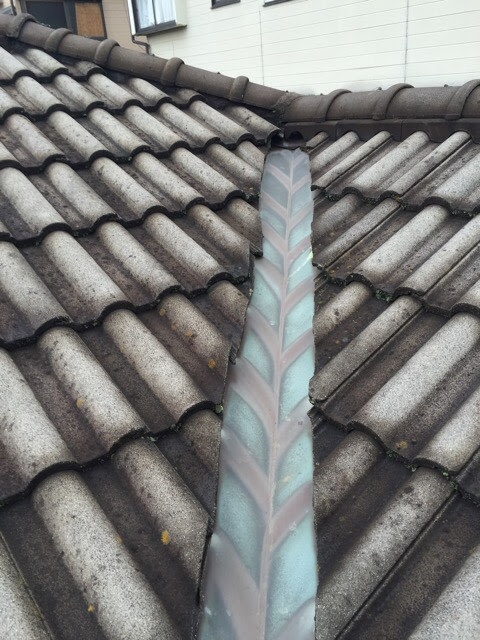 屋根の谷間を通る銅製の谷板金。全体的に変色し、劣化が進んでいる様子。