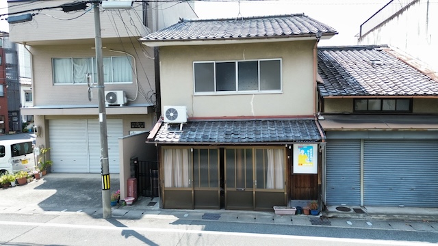 現場調査時の建物全景写真。築年数が経過した日本瓦の屋根と、1階下屋根の状況をドローンで撮影