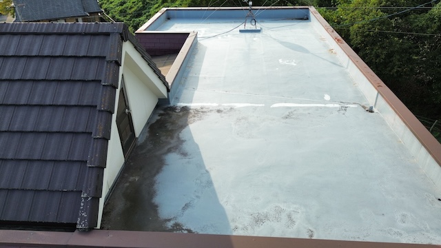 ベランダ（陸屋根）の防水層表面。全体的に黒ずみや色褪せが発生しており、トップコートの保護機能が低下して防水メンテナンスが必要なサインが出ている。