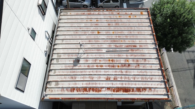 真上から撮影した金属屋根（折板屋根）のドローン画像。縞模様のように錆が全体に広がっており、防水性の低下と劣化の進行具合が明確に分かる。