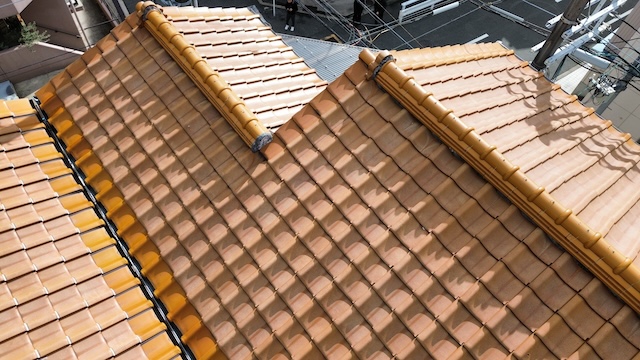 「京都市西京区の3階建て住宅にてドローン屋根点検。過去に部分補修された瓦屋根の範囲。既存の古い瓦と、新しく積み直された部分（色の明るい箇所）の違いを確認し、全体葺き替えの必要性を診断」