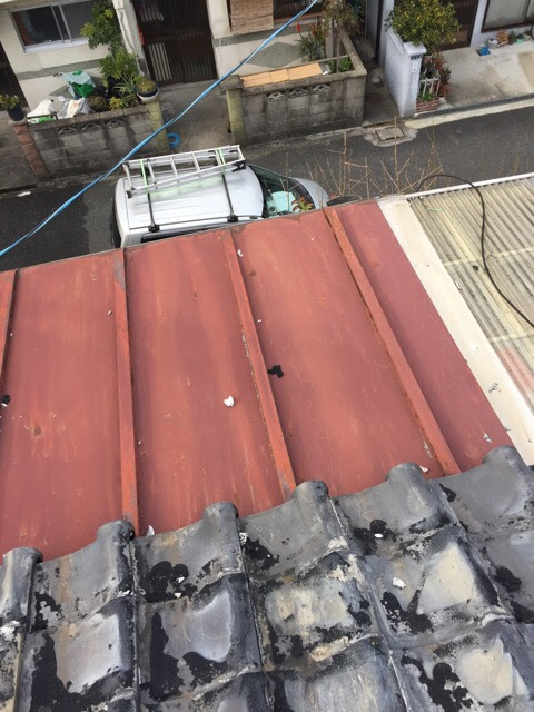 瓦屋根に隣接する金属製のトタン屋根。全体的に赤茶色に錆びており、老朽化が進んでいる状況。