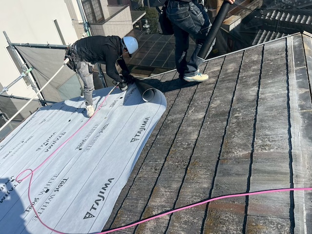 高耐久な粘着系防水シートであるタディスホワイトを既存屋根に張り込む施工風景