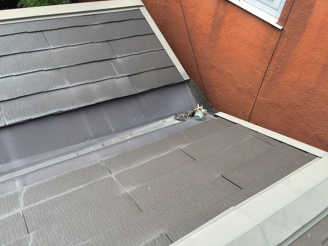 渡辺： 「ここや。この**『雨押さえ板金』**、サビっサビやんけ。新品の屋根に対して、こんなボロい板金使い回すとか正気か？」  吉岡： 「おっしゃる通りですわ。屋根材が変われば厚みも変わるし、本来なら板金も新しく作り直さなあかんとこですよね。」  渡辺： 「当たり前やろ！ これじゃあ、新しい屋根と古い板金の間に隙間ができるに決まっとる。 『屋根屋』名乗るんやったら、ここを現場に合わせてカンカン叩いて納めるんが仕事やろが。それをやらへんとか、職人の風上にも置かれへんで。」